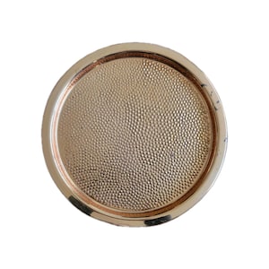 May include: A round, gold-colored tray with a textured, dotted surface. The tray has a raised rim and a shiny finish. The design is simple and elegant, suitable for serving or display.