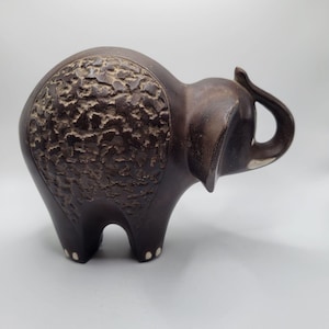May include: A dark brown ceramic elephant figurine with a textured back and white accents on the feet and trunk.