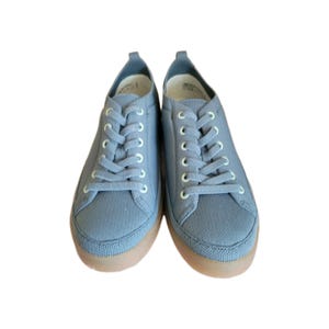 以下が含まれることがあります： 白い靴紐が付いた、明るい青色のキャンバススニーカーのペア。靴は、丸いつま先と茶色のラバーソールを備えたロープロファイルデザインです。 スニーカーは新品で清潔です。