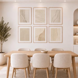 Può includere: Un set da pranzo con un tavolo rettangolare in legno chiaro e sei sedie imbottite in una tonalità beige neutra. Sulla parete, sei cornici quadrate mostrano texture beige astratte e linee. Una pianta alta in vaso si trova sulla sinistra.
