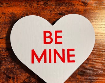 May include: White heart-shaped sign with the words "BE MINE" in red lettering.