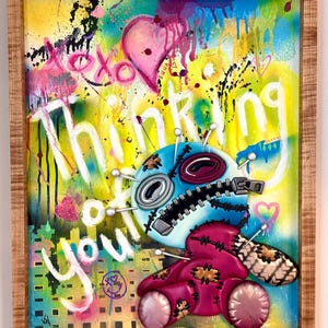 May include: A colorful, abstract painting with a 3D, stitched, blue and pink doll with pins. The text "Thinking of you" is written in white paint on a yellow background.