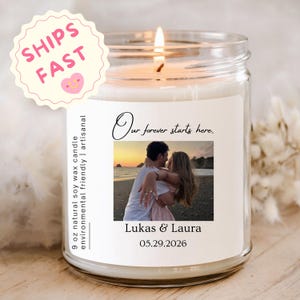 May include: A clear glass jar candle with a white label featuring a photograph of a couple on a beach, the text Our forever starts here, the names Lukas & Laura, the date 05.29.2026, and the text 9 oz natural soy wax candle environmental friendly.