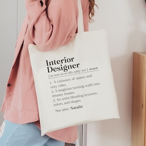 May include: A white tote bag with black text that reads "Interior Designer" and a definition of the word. The definition includes the phonetic spelling of the word and a list of three characteristics of an interior designer. The text also includes the name "Natalie".