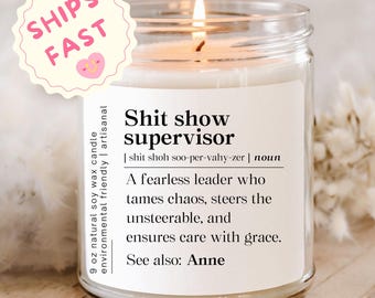 May include: A lit soy wax candle in a clear glass jar. The label reads "Shit show supervisor" with a definition. A pink and white sticker with the words "Ships Fast" is in the upper left corner. The candle is 9 oz.