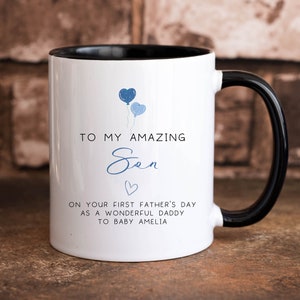 May include: White ceramic mug with a black rim and handle. The mug has a blue heart balloon design and the text "To my amazing Sen". Below the text is a small heart and the text "On your first Father's Day as a wonderful Daddy to baby Amelia."