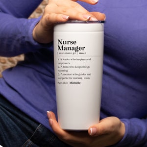 May include: White travel mug with a black design that reads "Nurse Manager" and defines the term as a leader, hero, and mentor. The mug also says "See also: Michelle".