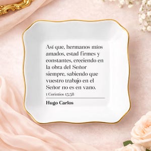 May include: A square white ceramic trinket dish with scalloped edges and a gold-painted rim. The center features black printed text in Spanish reading: Así que, hermanos míos amados, estad firmes y constantes, 1 Corintios 15:58, Hugo Carlos.