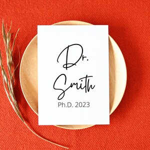 May include: A white card with black text that reads "Dr. Smith Ph.D. 2023" on a wooden plate and a red background.
