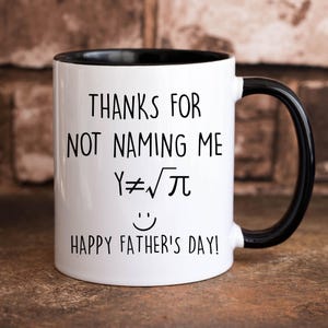 May include: White coffee mug with a black rim and handle. The mug has black text that reads "Thanks for not naming me Y≠√π Happy Father's Day!"