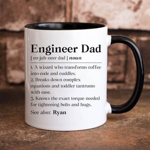 May include: A white ceramic mug with a black interior and handle, featuring black printed text that defines Engineer Dad as a wizard who transforms coffee into code and cuddles, breaks down complex equations, and knows torque for bolts.
