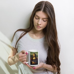 Könnte beinhalten: Weiße Keramiktasse mit einem bunten Bild der Mona Lisa und dem Text "Also, das ist ein Meisterwerk, ja? Gern geschehen. - Leonardo da Vinci".