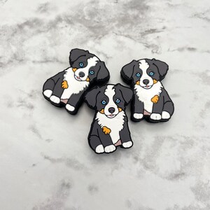 May include: Three black and white Bernese Mountain Dog puppy figurines with blue eyes. The figurines are sitting on a white marble surface.