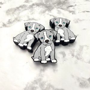 May include: Three gray and white pit bull puppy figurines with blue eyes. The figurines are sitting on a white marble surface.