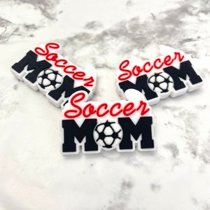 May include: Three black and white "Soccer Mom" charms with a red "Soccer" inscription and a soccer ball graphic.