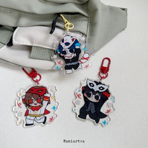 Peut inclure: Trois porte-clés en acrylique représentant des personnages de style anime avec des masques. Les porte-clés ont des fermoirs rouges et sont attachés à un sac vert clair. Les personnages sont dans diverses poses et tenues, avec des accents colorés.