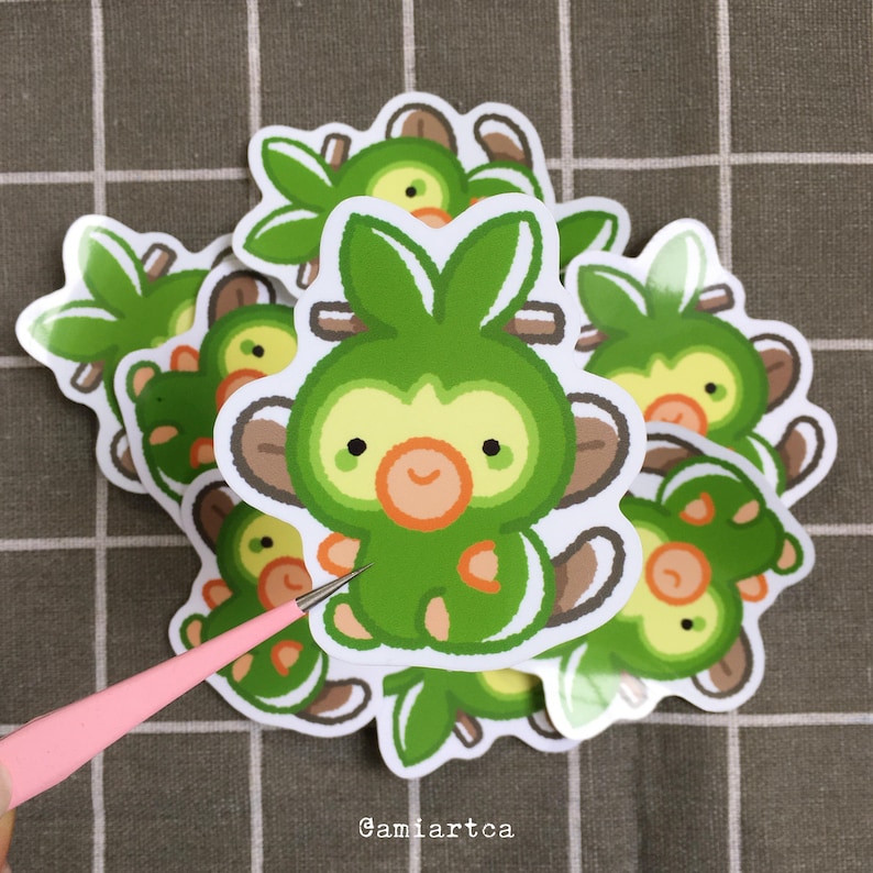 Pode incluir: Uma cole&ccedil;&atilde;o de autocolantes de macacos de desenho animado verdes e amarelos com detalhes castanhos e tra&ccedil;os faciais laranja. Os autocolantes est&atilde;o numa superf&iacute;cie xadrez castanha e branca. O texto "Gamiartca" &eacute; vis&iacute;vel na parte inferior.