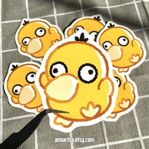 Pode incluir: Uma cole&ccedil;&atilde;o de adesivos de pato amarelo de desenho animado com olhos pretos e brancos e detalhes em laranja. Os adesivos est&atilde;o em uma superf&iacute;cie xadrez cinza e branca. O texto "amiartea.etsy.com" &eacute; vis&iacute;vel.