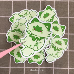 Pode incluir: Uma cole&ccedil;&atilde;o de autocolantes verde claro com um design de gato de desenho animado e detalhes em verde escuro. Os autocolantes t&ecirc;m uma borda branca e est&atilde;o empilhados. O texto "Gamiartca" &eacute; vis&iacute;vel. Os autocolantes t&ecirc;m um design fofo e divertido.