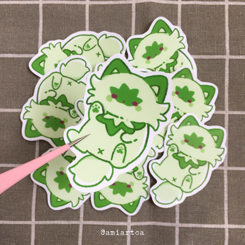 Pode incluir: Uma cole&ccedil;&atilde;o de autocolantes verde claro com um design de gato de desenho animado e detalhes em verde escuro. Os autocolantes t&ecirc;m uma borda branca e est&atilde;o empilhados. O texto "Gamiartca" &eacute; vis&iacute;vel. Os autocolantes t&ecirc;m um design fofo e divertido.