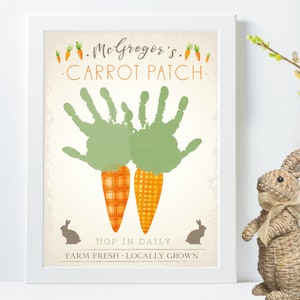 Puede incluir: Una impresión enmarcada con un diseño de huerto de zanahorias hecho con huellas de manos. La impresión presenta dos huellas de manos verdes con zanahorias de cuadros naranja y blanco. El texto en la impresión dice "McGregor's Carrot Patch. Hop in daily. Farm Fresh - Locally Grown."