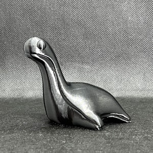 May include: A silver-colored, stylized sculpture of a long-necked creature with a rounded head. The sculpture is smooth and has a metallic sheen.