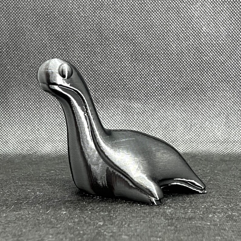 May include: A silver-colored, stylized sculpture of a long-necked creature with a rounded head. The sculpture is smooth and has a metallic sheen.