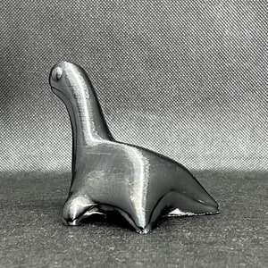 May include: A silver-colored, stylized dinosaur figurine. The dinosaur is standing on all fours with its head raised.