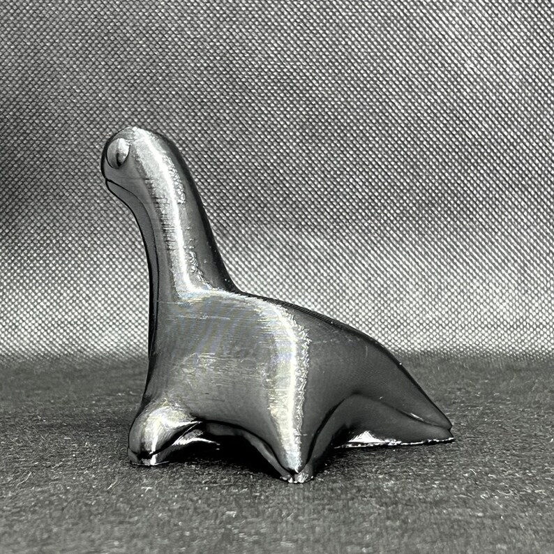 May include: A silver-colored, stylized dinosaur figurine. The dinosaur is standing on all fours with its head raised.