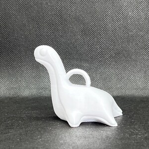 May include: White plastic dinosaur ornament with a loop for hanging. The dinosaur is in a sitting position with its head tilted up.