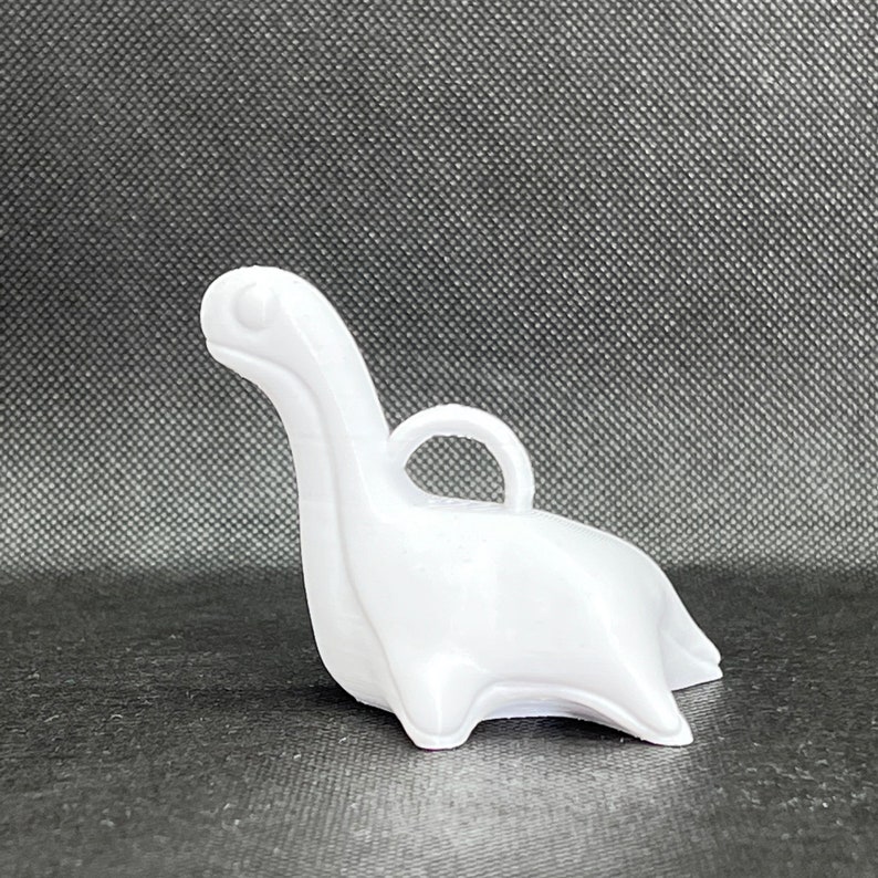 May include: White plastic dinosaur ornament with a loop for hanging. The dinosaur is in a sitting position with its head tilted up.