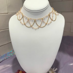 May include: A gold chain choker necklace with pink beads. The necklace has a layered design with multiple strands of chain and beads.