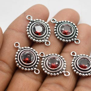 May include: Five silver-toned pendant connectors with red gemstone accents. Each connector has two loops for attaching to jewellery.