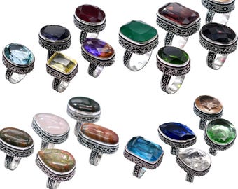 May include: Collection of gemstone rings with various colored stones, including blue, green, red, and yellow. The rings have ornate silver-colored bands. The gemstones are oval, rectangular, and round.
