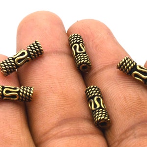 May include: Five gold-toned metal beads with a decorative pattern. The beads are cylindrical and have a textured surface.