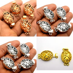 Op de afbeelding: Een assortiment ovale sieraden sluitingen in goud, zilver en koper tinten. De sluitingen hebben een sierlijk, opengewerkt ontwerp. De sluitingen worden in verschillende groepen getoond, sommige open en andere gesloten.