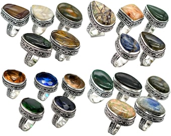May include: A collection of gemstone rings with various shapes and colors. The rings have ornate silver-toned bands and feature stones in shades of brown, green, blue, and other earth tones. The gemstones are oval, teardrop, and square shaped.