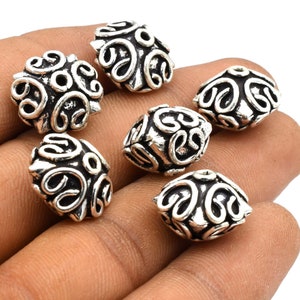 May include: Six silver-toned metal beads with intricate, swirling designs. The beads are square-shaped with rounded edges.