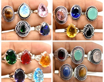 May include: A collection of 12 silver rings with various gemstone settings. The rings feature a variety of colors, including green, red, blue, yellow, pink, and purple. The gemstones are set in a variety of styles, including pear-shaped, oval, and round.