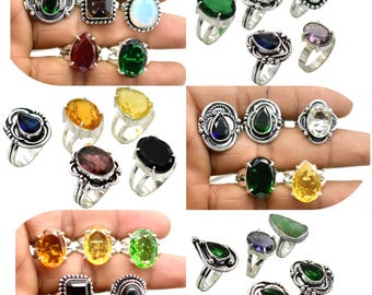May include: A collection of gemstone rings in various shapes and colors, including green, brown, blue, and yellow. The rings have silver bands and are displayed on a hand. The gemstones are oval, pear, and rectangular shaped.