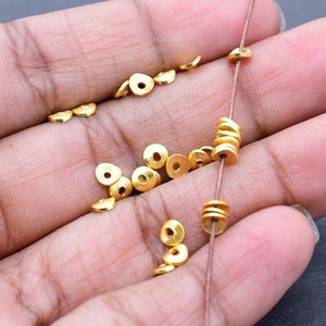 May include: A close-up of a hand holding a string of gold-coloured metal beads. The beads are small and round, and they are arranged in a circular pattern. There are also several loose beads scattered around the hand.