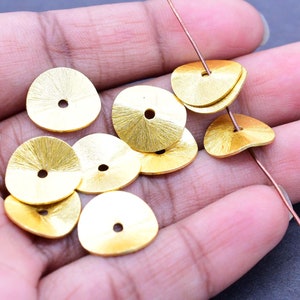 May include: A collection of gold-coloured metal beads with a textured surface and a hole in the centre. The beads are arranged in a hand, with some stacked on top of each other.