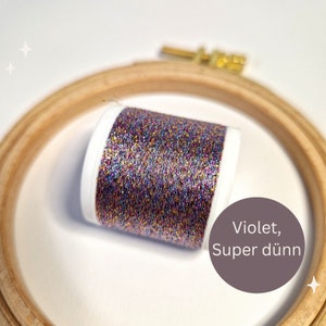 Könnte beinhalten: Eine Spule mit metallischem Stickgarn in verschiedenen Farben, darunter Lila, Gold und Silber. Das Garn ist sehr fein und hat einen glitzernden Schimmer. Das Etikett auf der Spule lautet "Violet, Super dünn".