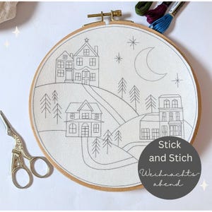 Könnte beinhalten: Ein Stickrahmen mit einem handgestickten Landschaftsdesign. Das Design umfasst Häuser, Bäume, einen Halbmond und Sterne, alles in grauer Farbe auf weißem Stoff. Der Text "Stick and Stich Weihnachtsabend" befindet sich in einem Kreis. Eine goldene Schere befindet sich links.