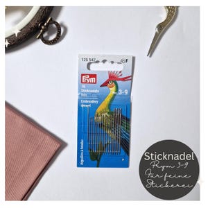 Könnte beinhalten: Eine blaue und grüne Packung mit 16 feinen Sticknadeln der Größe 3-9 von Prym. Die Packung zeigt eine bunte Vogel-Illustration und den Text "Sticknadel Prym 3-9 Fur feine Stickerei".