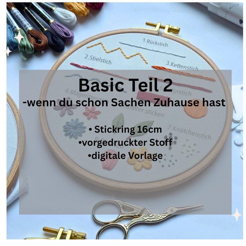 May include: An embroidery hoop with a printed fabric design, featuring various stitch examples and floral patterns. The text "Basic Teil 2" is displayed, along with "Stickring 16cm" and other details. A pair of gold scissors is in the foreground.