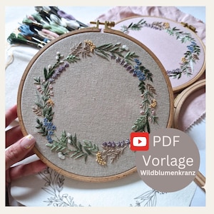May include: Close-up of embroidered floral wreaths in wooden hoops. The wreaths feature green leaves, purple, blue, and yellow flowers. The text "PDF Vorlage Wildblumenkranz" is visible in the lower right corner. Embroidery floss is visible in the background.