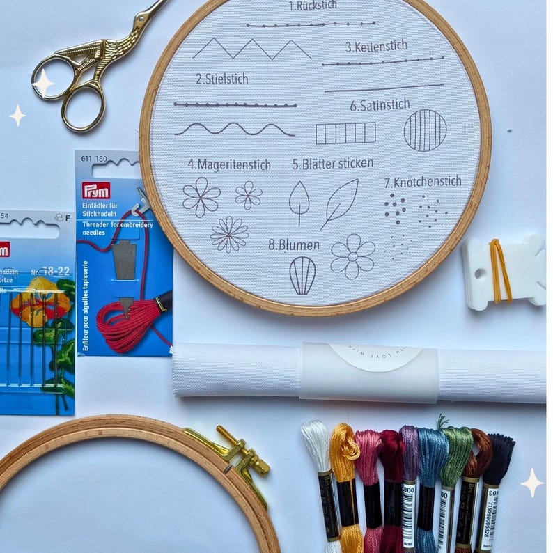 May include: Embroidery kit with a wooden hoop, scissors, needles, and colorful threads. A white fabric hoop displays stitch examples with German labels. Includes a needle threader and a roll of white fabric.