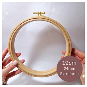 Könnte beinhalten: Ein Holz-Stickrahmen mit einem Durchmesser von 19 cm und einem 24 mm breiten Rand. Der Rahmen ist aus Naturholz gefertigt und hat einen Messing-Schraubverschluss.