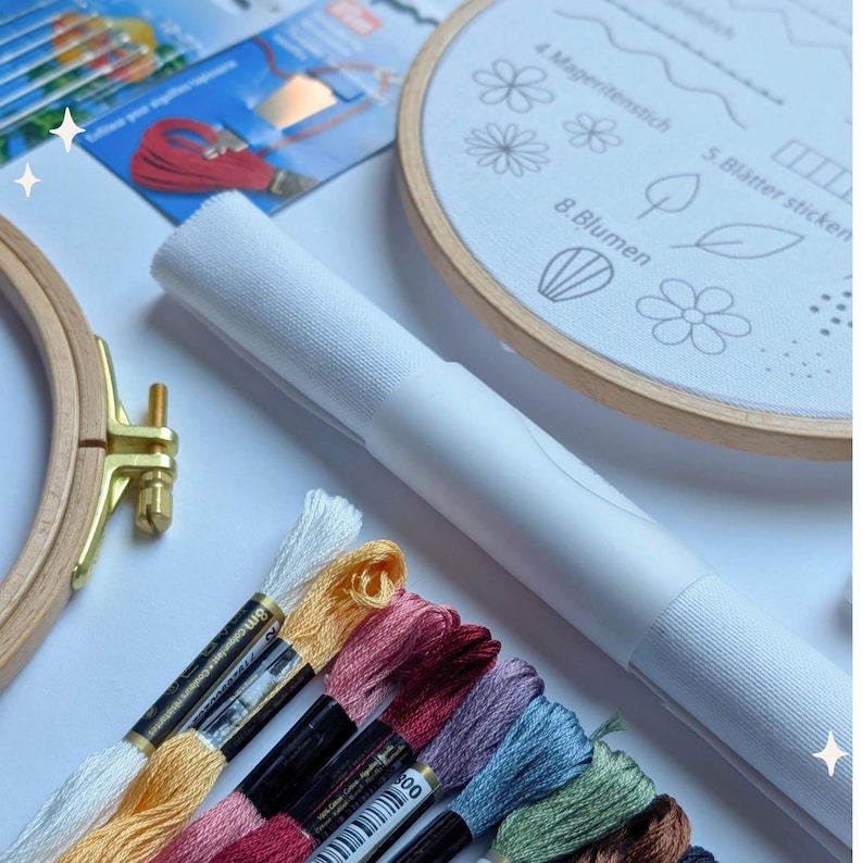 May include: Embroidery kit with a wooden hoop, colorful embroidery floss, and a white fabric with floral pattern designs. A white cylindrical object is also present, along with other crafting supplies.